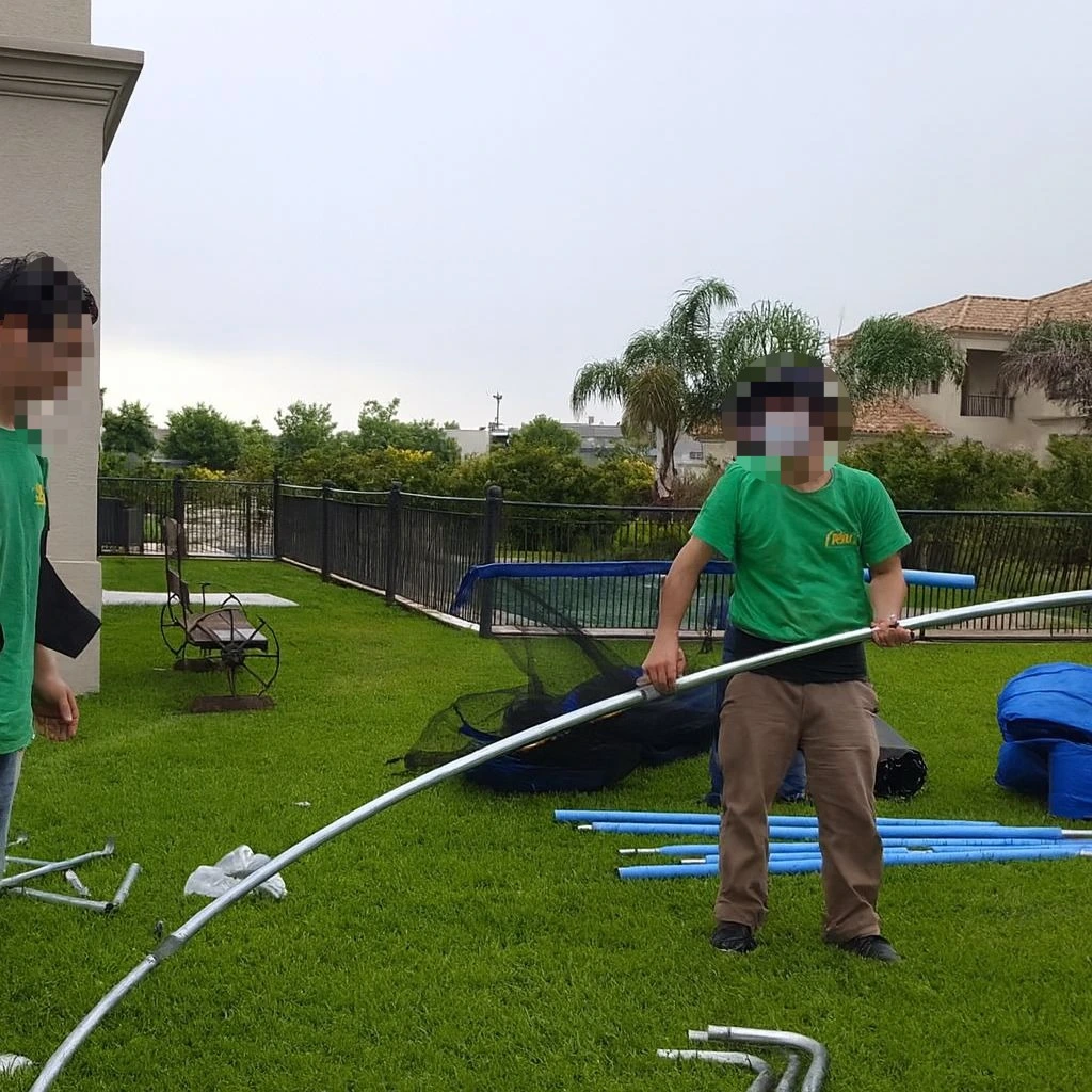 Personal de mudanzas realizando el desarme de la estructura metálica de una cama elástica en el jardín de una casa en barrio cerrado para su traslado.